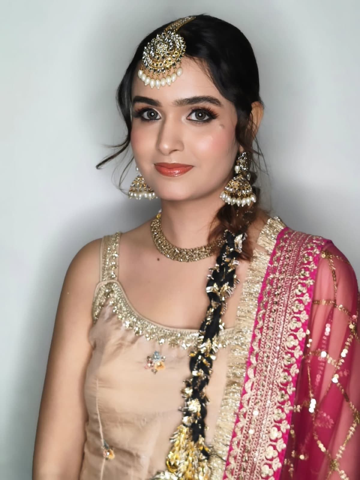 Bridal makeup with warm glowy skin, soft smokey eyes, and coral lips on a bride in a champagne lehenga with hot pink dupatta
