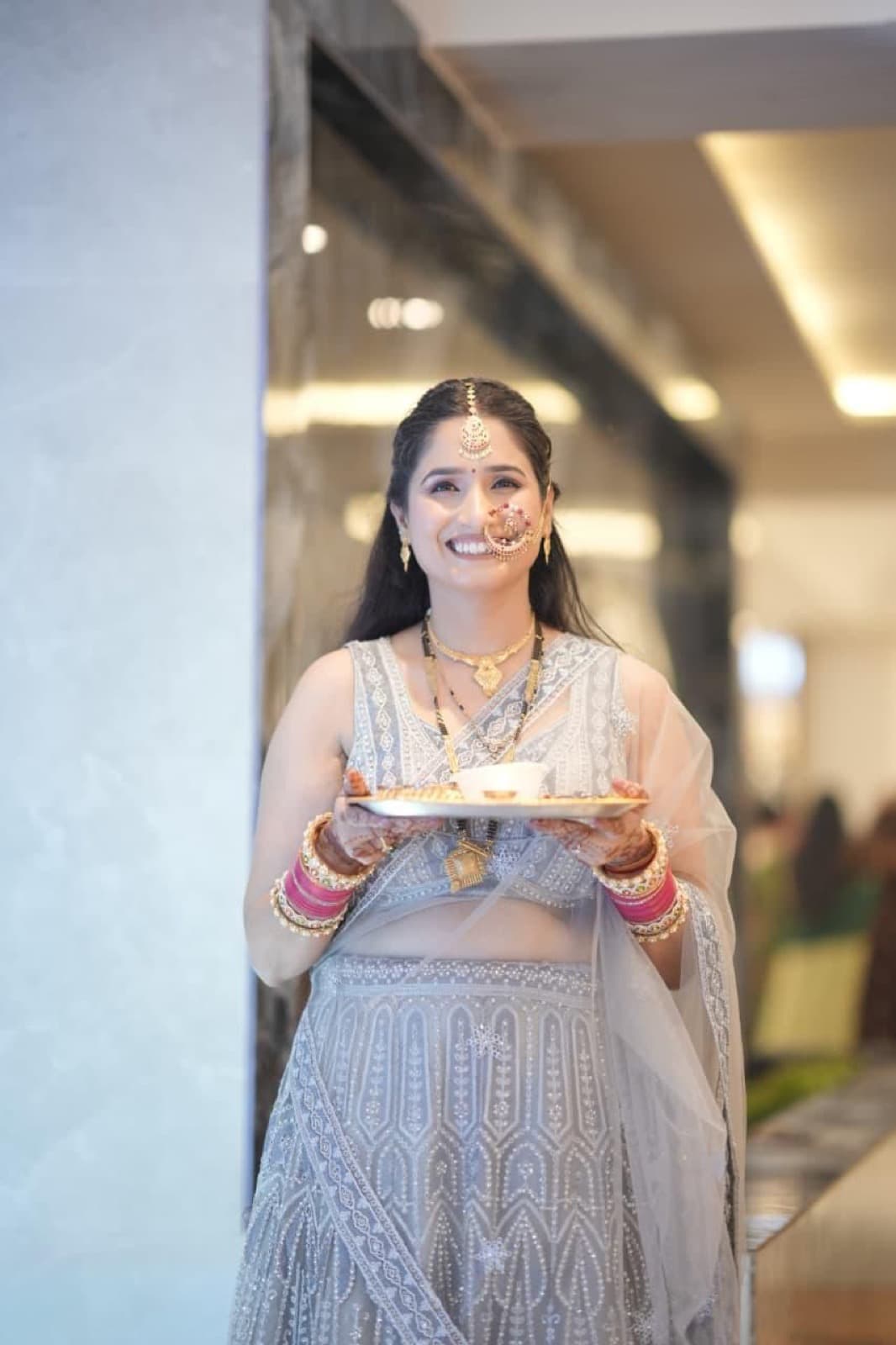 Bridal portrait with glowing skin and soft smokey eyes on a bride in a grey embroidered lehenga holding a puja thali, smiling