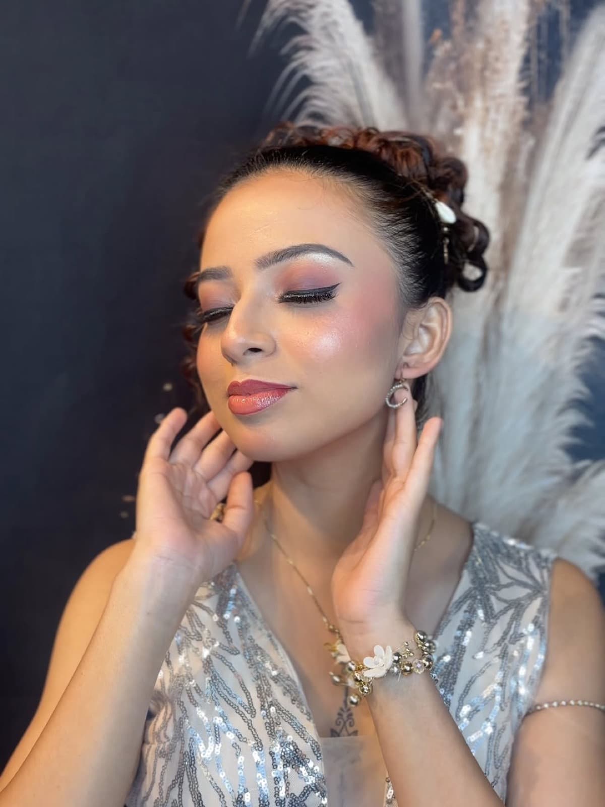 Soft glam party makeup with peach eyes, contoured skin, and nude lips on a client in a silver sequin dress