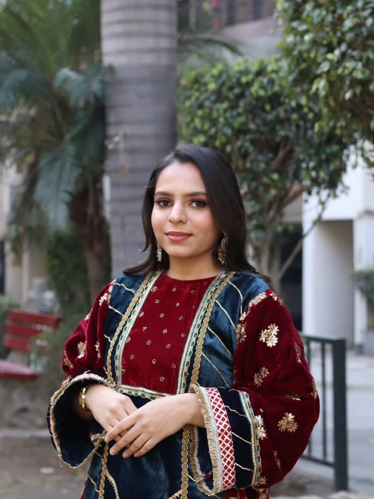Natural festive makeup with soft eyes and berry lips on a client in a maroon velvet embroidered suit, garden backdrop