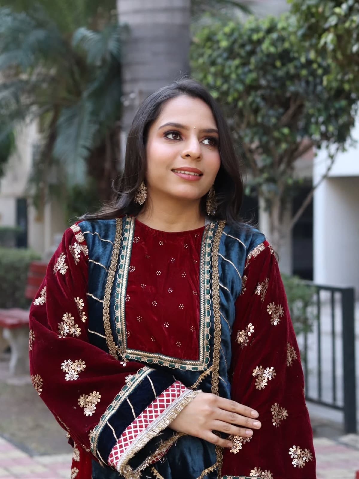 Fresh festive makeup with natural glow on a client in a maroon and teal embroidered velvet salwar suit, outdoors