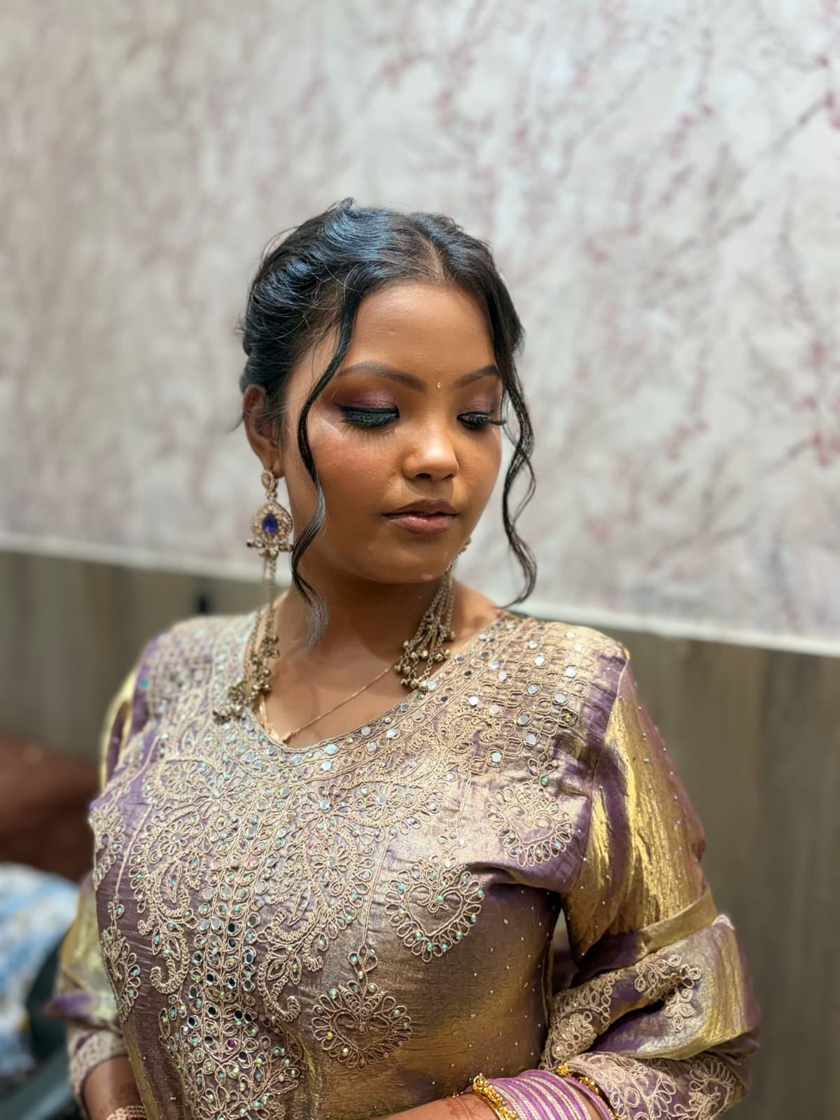 Bridal makeup with defined eyes and subtle lip on a client in a lavender and gold lehenga, eyes cast down