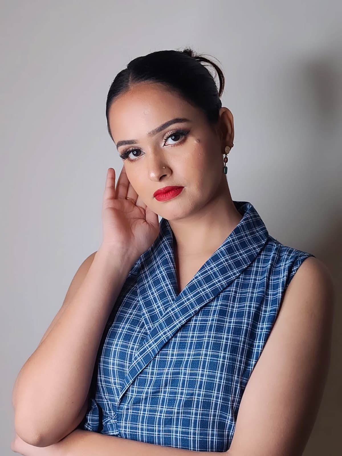 Bold red lip and sharp winged liner editorial look on a client in a blue plaid sleeveless blazer dress, facing camera