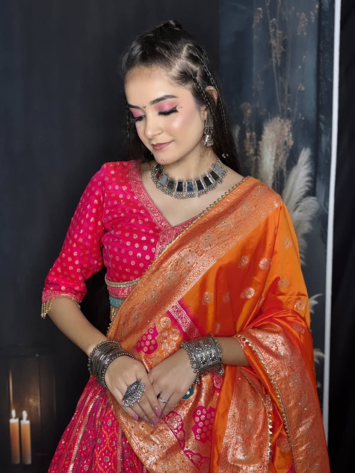 Navratri glam with rose pink eye makeup, braids, silver mirror necklace, and pink and orange banarasi lehenga with candle-lit backdrop