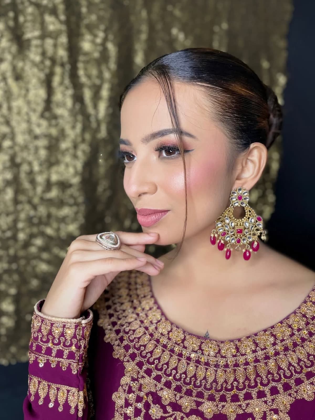 Elegant engagement look with rose gold shimmer eyes, sleek bun, kundan and ruby chandbali earrings, on a model in a plum embroidered suit