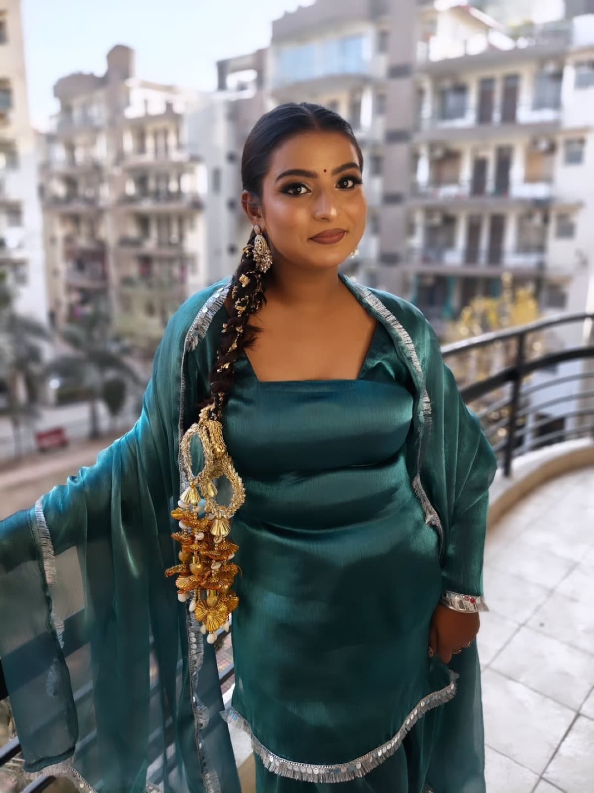 Festive glam makeup with defined eyes and teal silk lehenga on a client with kaleere and chandelier earrings, standing on a balcony