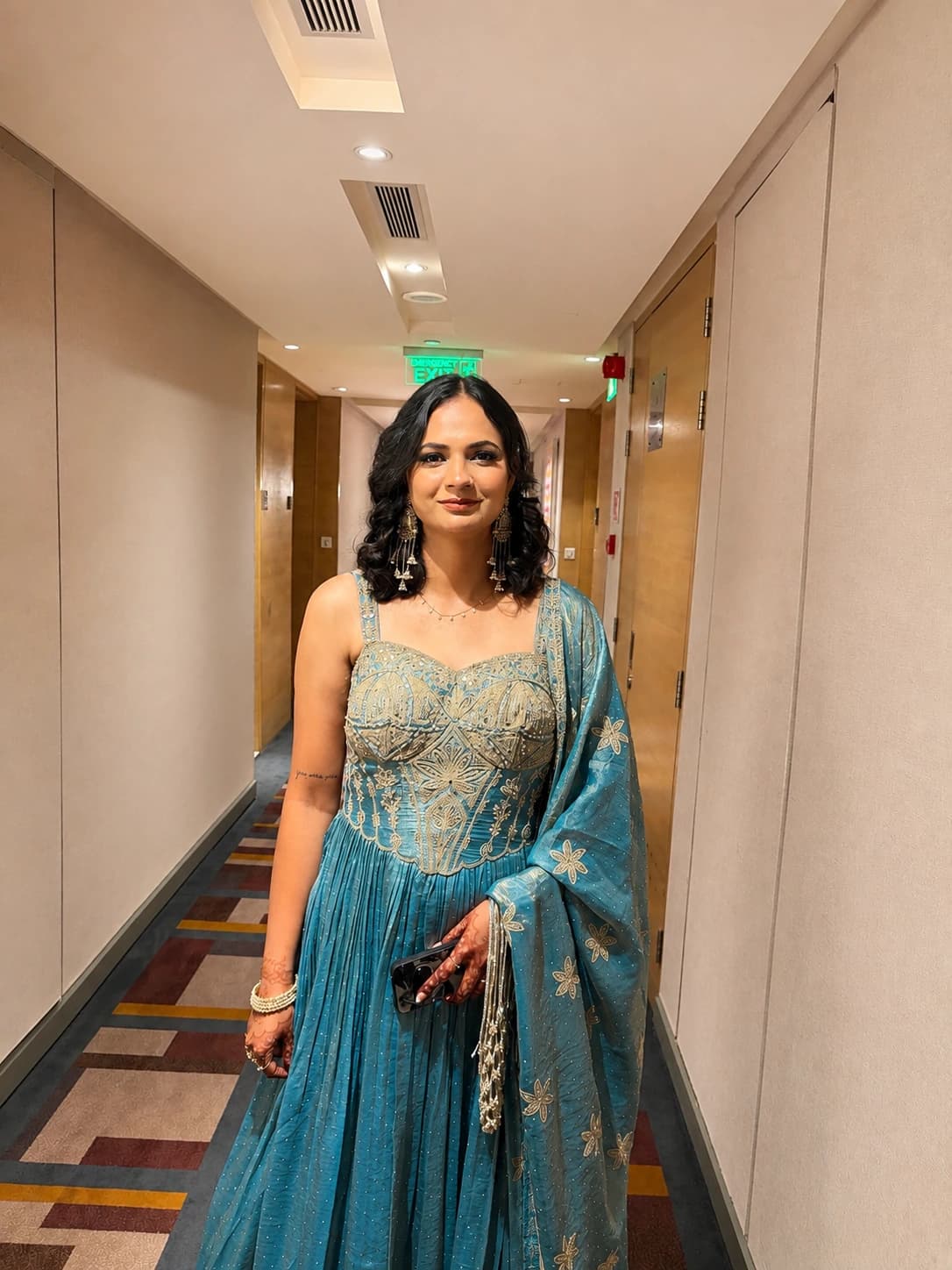 Full-length party portrait with softly defined eyes, loose curls and a teal embroidered outfit