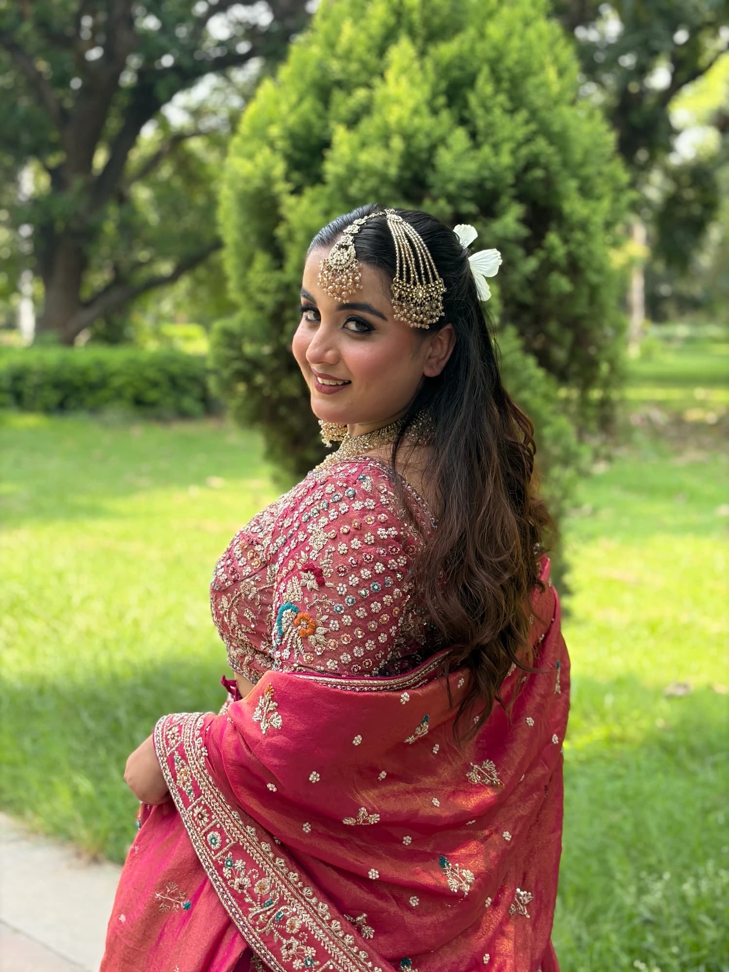 Side portrait with soft pink makeup and loose waves, wearing a pink embroidered outfit in a garden