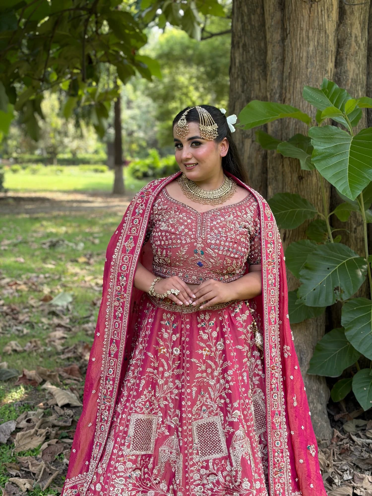 Full-length garden portrait with glowing makeup, gold jewellery and a pink embroidered outfit