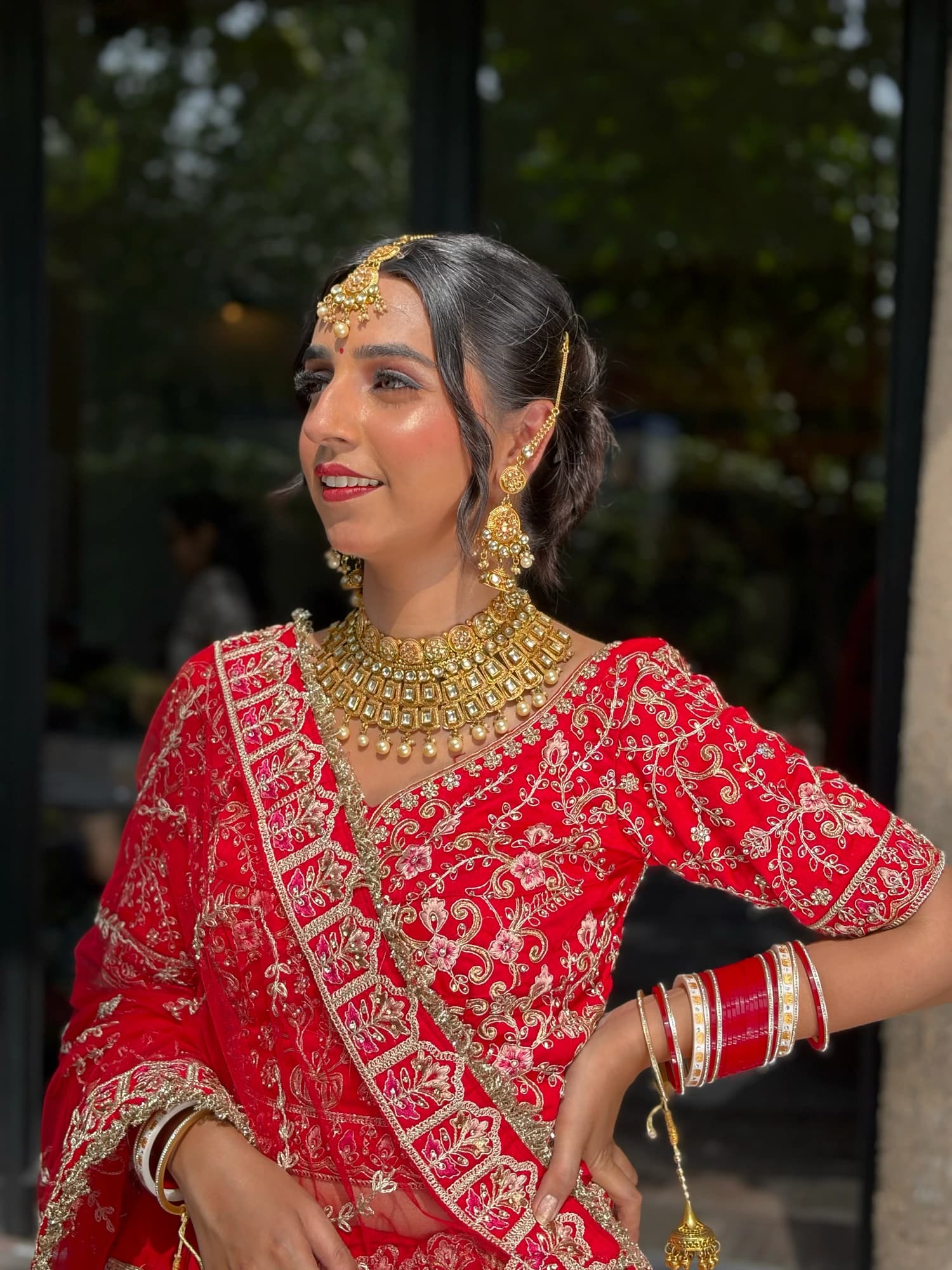 Smiling bridal side portrait with warm eyes, rose lips and a gold choker, wearing a red lehenga