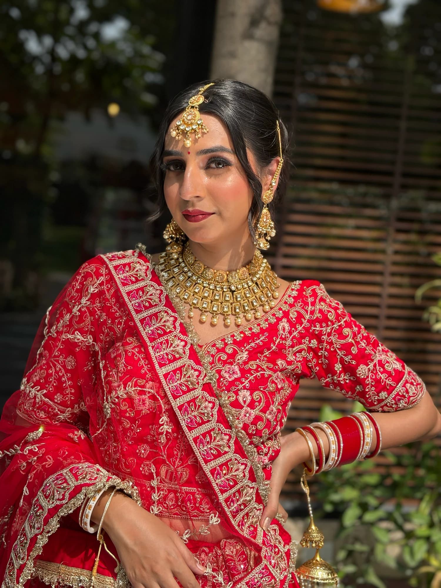 Bridal portrait with glowing cheeks, defined brows and rose lips, wearing a red lehenga and gold jewellery
