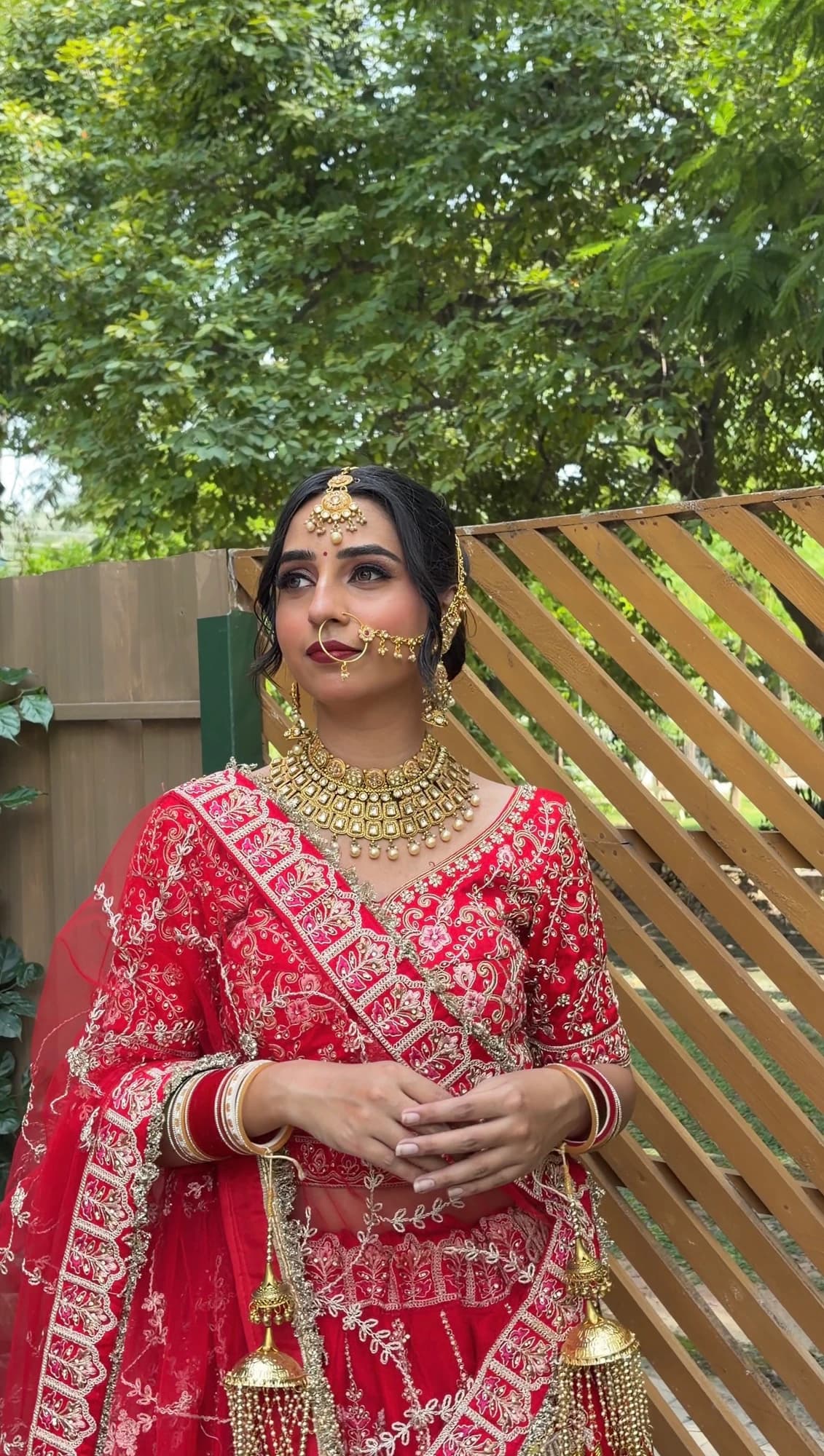 Bridal portrait with a gold nose ring, softly glowing makeup and layered jewellery, wearing a red embroidered lehenga