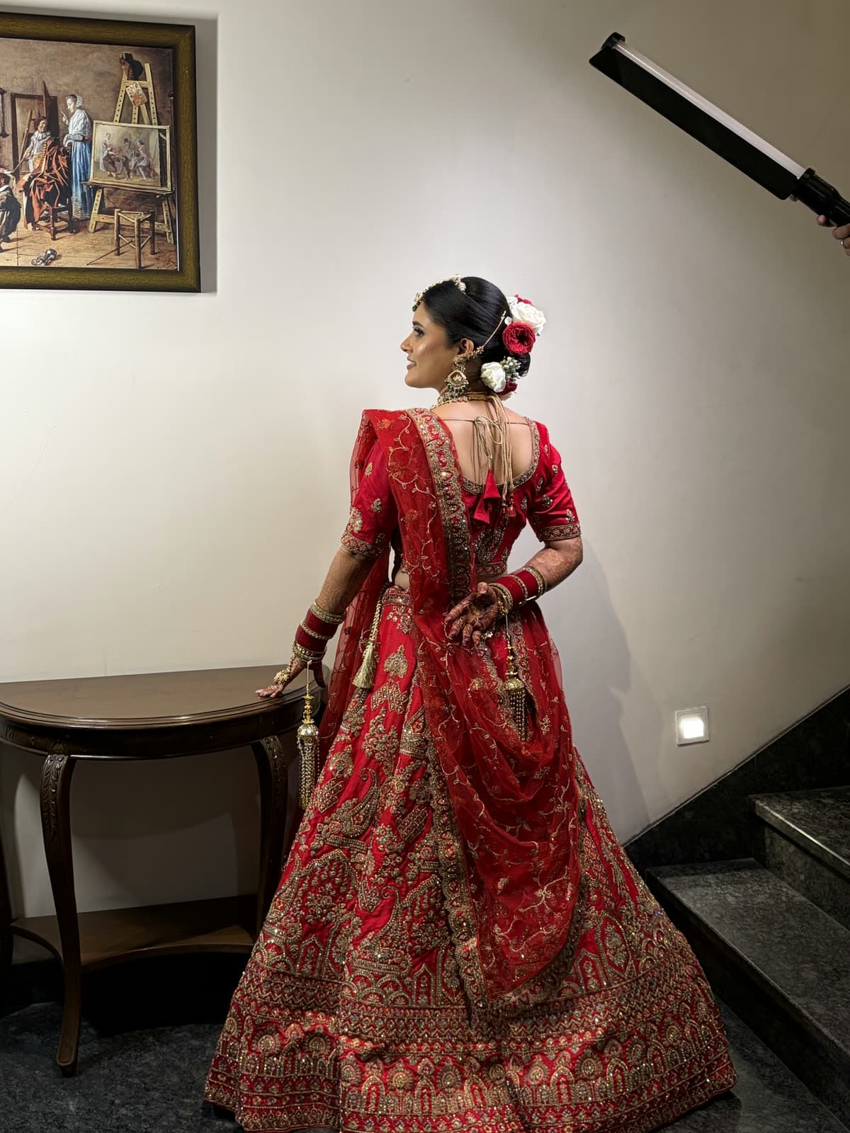 Back-profile bridal portrait showing a sleek floral bun, softly glowing makeup, and an embroidered red lehenga