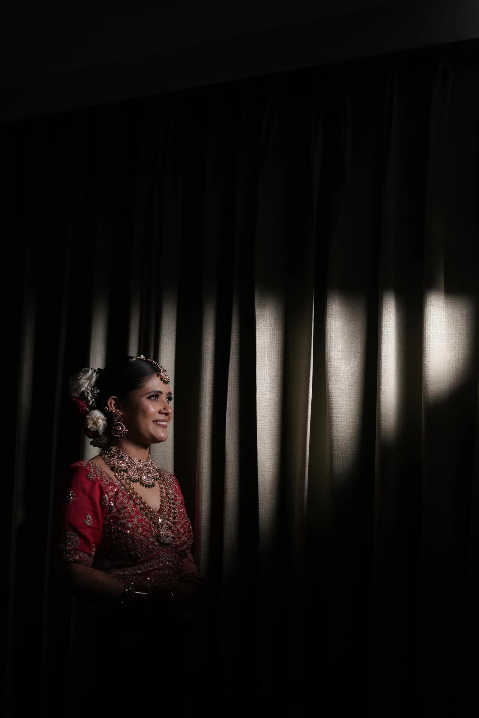 Shilpa in her finished red bridal look photographed beside dark curtains
